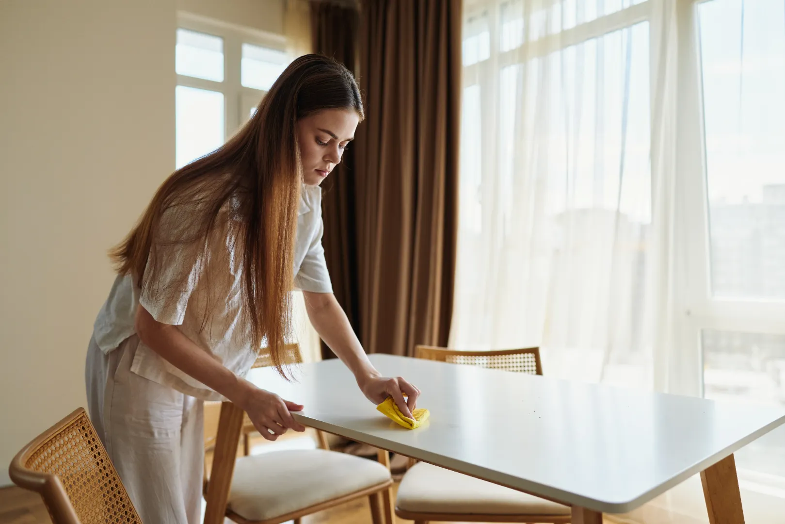 Woman cleaning a dining table with a cloth to remove dirt and surface residue.
