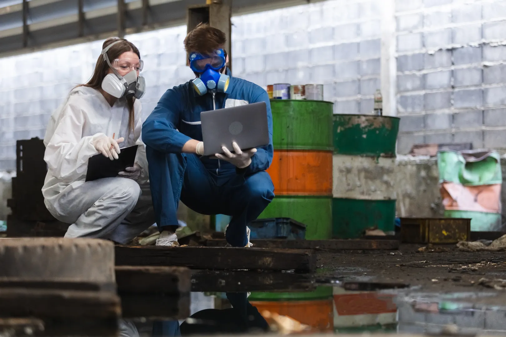 Two warehouse workers wearing protective masks assessing a hazardous material spill on the floor