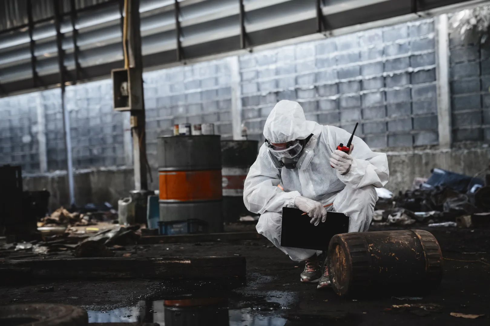 Hazardous material cleanup worker in protective clothing inspecting a chemical spill inside a warehouse