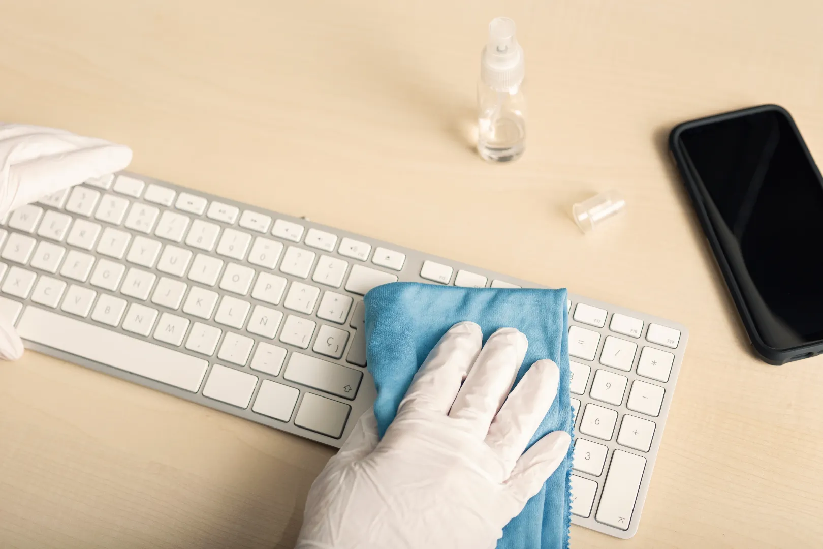 A person wiping a computer keyboard with a cleaning cloth