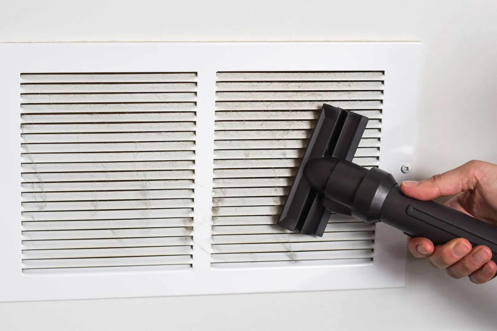 A person vacuuming dust from an air vent