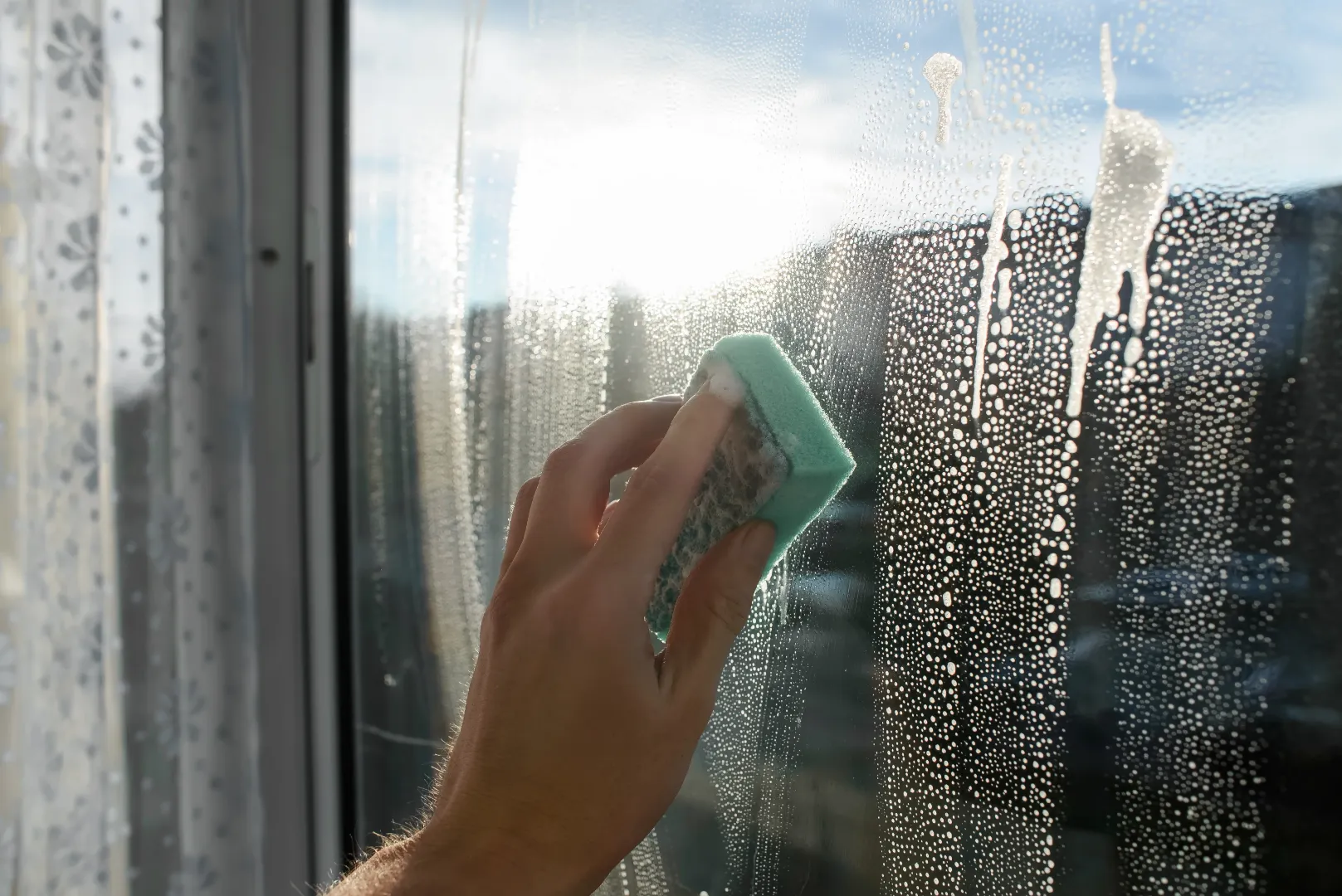 A person washing a window with a sponge and cleaning solution