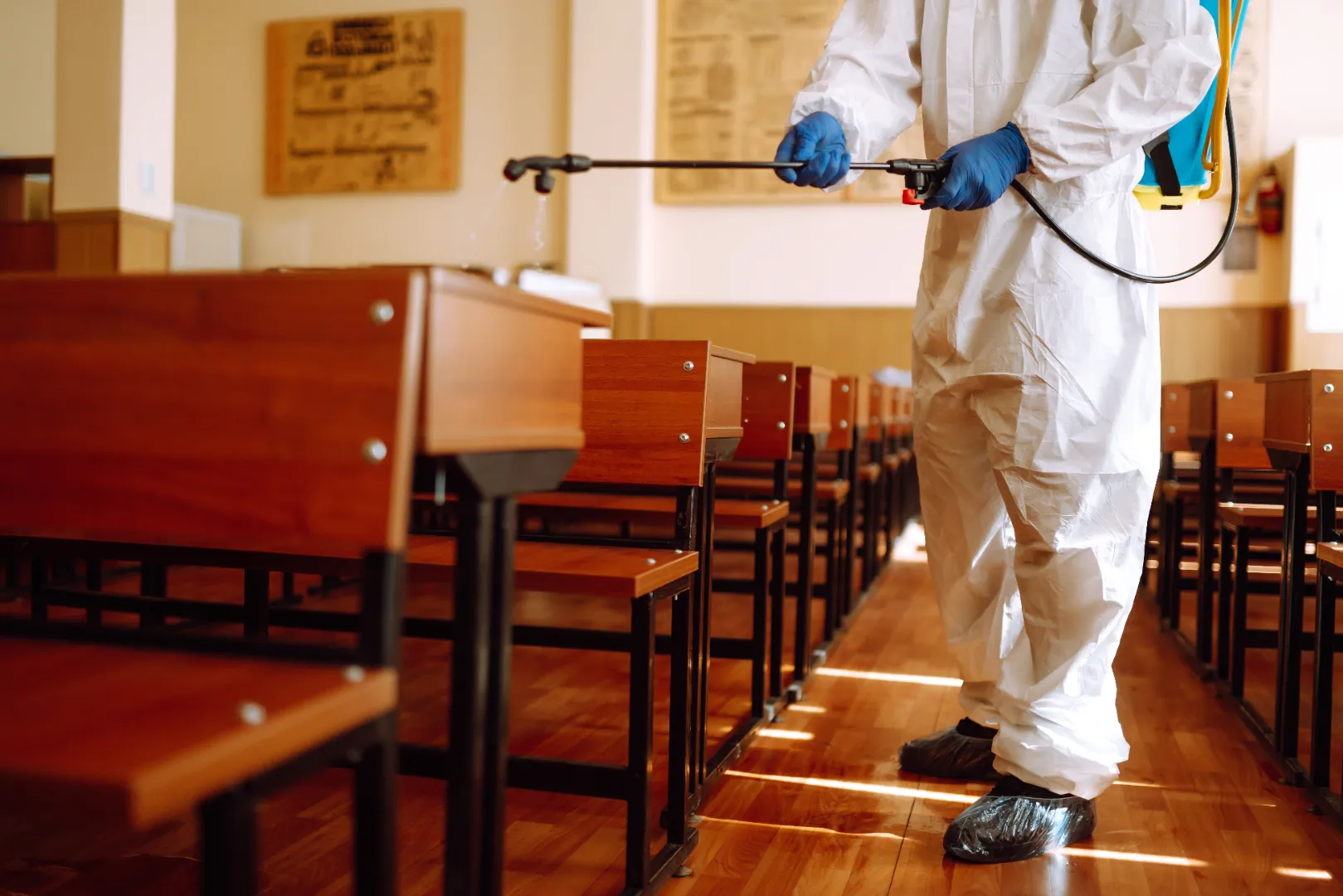 Worker using an electrostatic sprayer in a school classroom